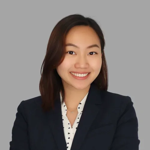 Elaine Luu smiling, with shoulder-length dark hair, wearing a dark blazer over a patterned light blouse against a gray background.