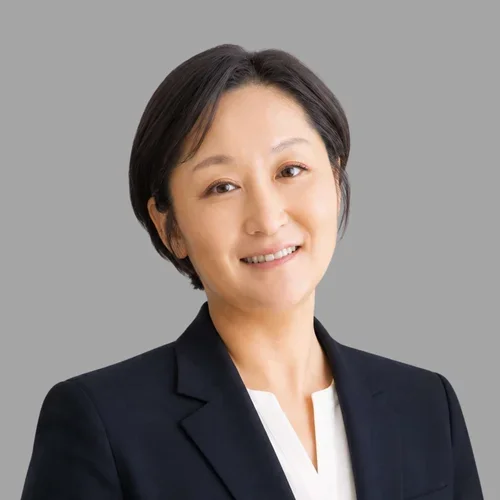 of Heidi Jang smiling, with short dark hair, wearing a dark blazer over a white top against a gray background.