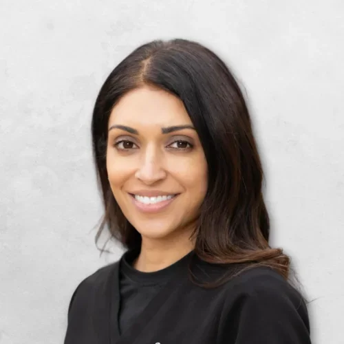 Dr. Radia has long brown hair and is wearing black scrubs