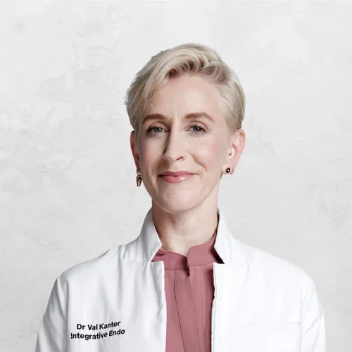 Dr. Val Kaner is wearing a white medical coat over scrubs.