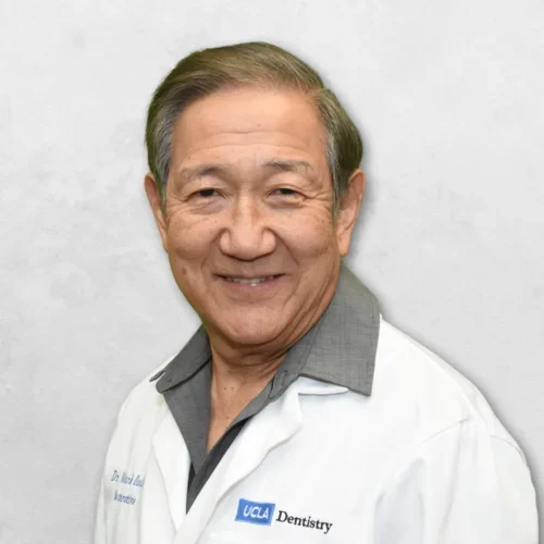 Dr. Ozaki is wearing a white doctor's coat over a gray shirt.