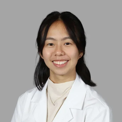 Yen Tung Lieu smiling, with dark hair pulled back, wearing a white coat over a light top against a gray background.