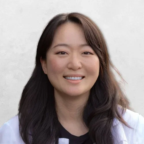 Michelle Jang has long brown hair and is wearing a white coat over a black top