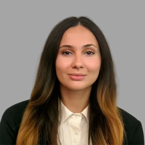 Golsa Veysi with long brown hair, wearing a dark blazer over a light blouse against a gray background.