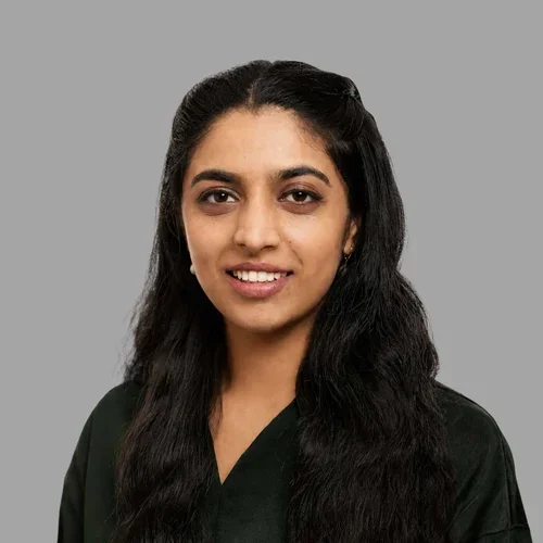 Sanchita Kashyap smiling, with long wavy dark hair, wearing a black top against a gray background.