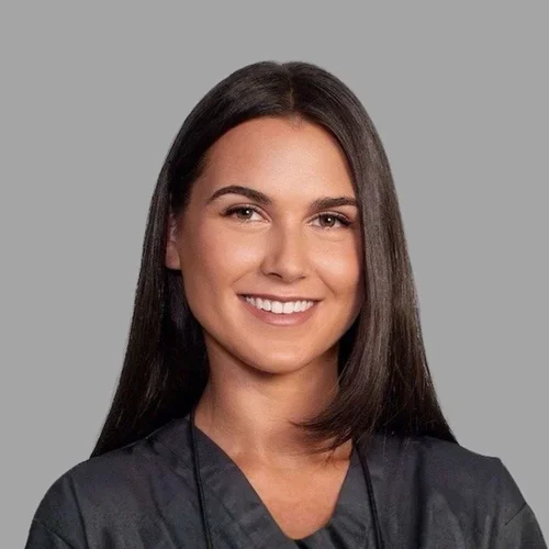 Rachel Brunswick smiling, with long straight brown hair, wearing dark scrubs against a gray background.