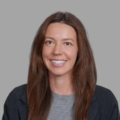 Jennifer Stodder smiling, with long straight brown hair, wearing a dark top against a gray background.