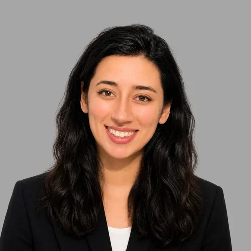 Paria Dehghanian smiling, with long dark hair, wearing a dark blazer over a light top against a gray background.