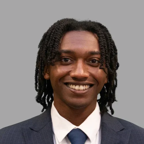 Dr. Kolbe Laing is wearing a dark pinstripe suit over a white shirt with a dark blue tie.