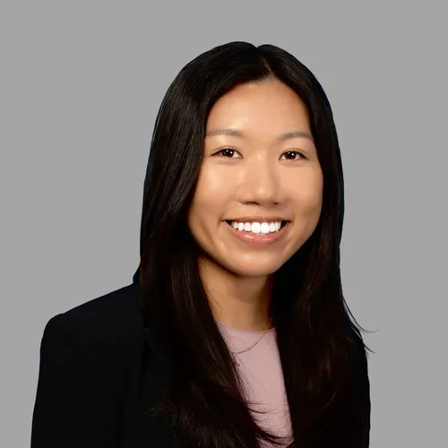Michelle Tong smiling, with long straight dark hair, wearing a black blazer over a light top against a gray background.