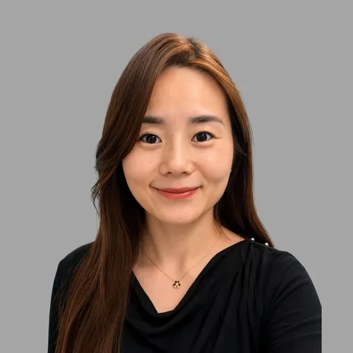 Ting Ruan with long dark hair swept to one side, wearing a black top and a subtle smile against a gray background.