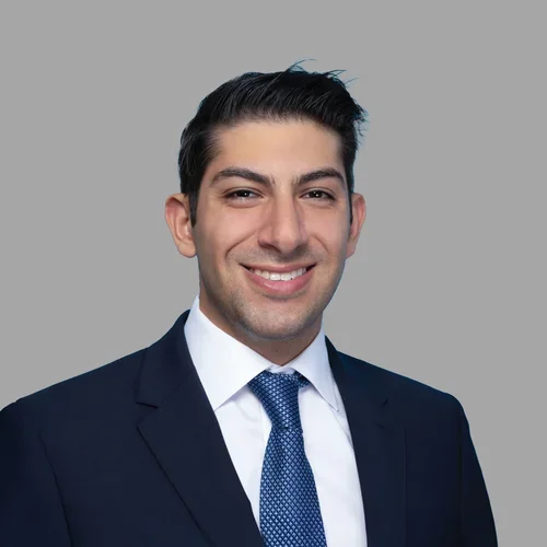 Dr. Mark Gettas is wearing a dark suit over a white collared shirt and a blue tie.