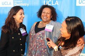 Three women laughing in front of a UCLA banner