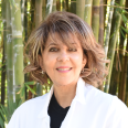 Dr. Mitra Elisha Simanian is wearing a white doctors coat over a black top