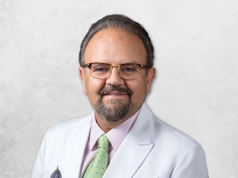 Saeid Razi is wearing glasses and a white doctor's coat over a pink shirt with a green tie