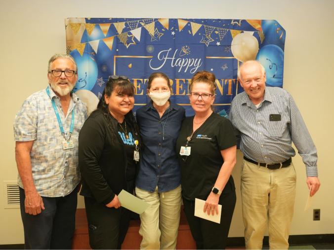 five people smiling in front of "happy retirement" sign