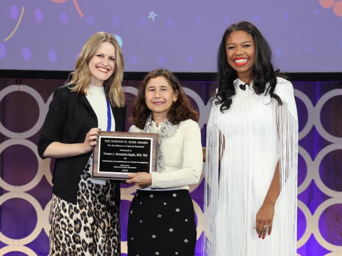 yvonne hernandez kapila accepting the Ross Award from two presenters.