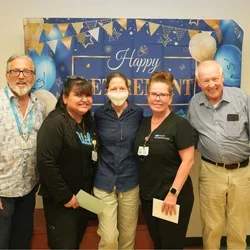 five people smiling in front of "happy retirement" sign