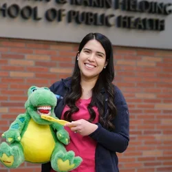 Damaris Arriola Zarate holding a dental education toy outside UCLA Fielding School of Public Health, representing community outreach and preventive care.