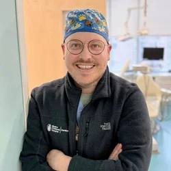 Joshua Vert in surgical cap and glasses standing in a clinical setting, representing specialized training in children’s oral health.
