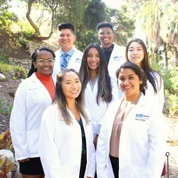 Seven people in white medical coats, standing in a botanical garden.