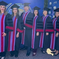 Six people in black graduation regalia against a blue backdrop