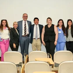 Group of nine people, some in medical scrubs and some in business attire, posing and smiling