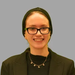 Medina Kerdjani, smiling, wearing glasses, a black headscarf, and black top against a gray background.