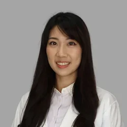 Kristi Lan smiling, with long straight dark hair, wearing a white coat against a gray background.