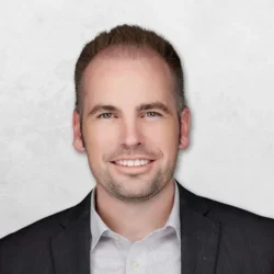 Andrei Marechek is wearing a black blazer over a white shirt and has short brown hair.