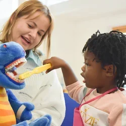 Woman showing child how to brush teeth using a stuffed animal