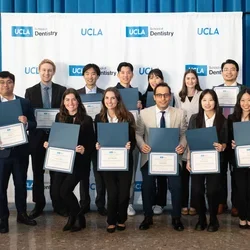 Group of 12 people holding award certificates, in front of UCLA School of Dentisrty-branded banner