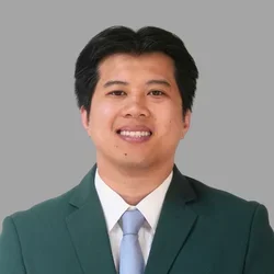 Anthony Nguyen smiling, with short dark hair, wearing a green suit jacket, white shirt, and light tie against a gray background.