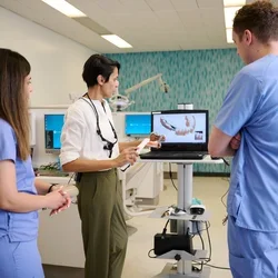 Instructor demonstrates intraoral scanning to two dental students in blue scrubs