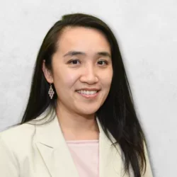 Dr. Wong is wearing a blazer over a pink shirt and has long, dark hair.