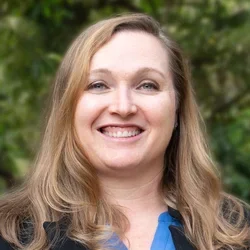 Dr. Owens is dressed in a black blazer layered over a blue blouse.