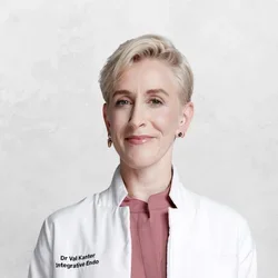 Dr. Val Kaner is wearing a white medical coat over scrubs.