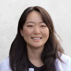 Michelle Jang has long brown hair and is wearing a white coat over a black top