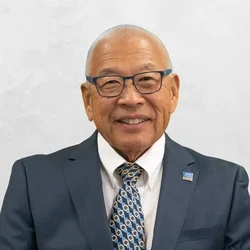 Dr. Ronaldo Mito is wearing a suit and tie over a white collared shirt.