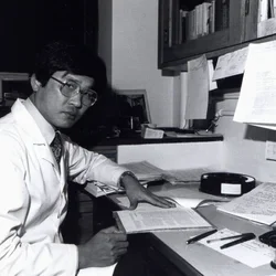 No-Hee Park in Lab coat, sitting at desk.