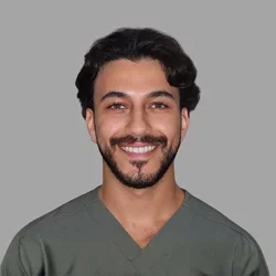 Abdelrahman Yousef smiling, with dark wavy hair and a short beard, wearing green scrubs against a gray background.