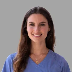 Caitlin Mispagel smiling, with long brown hair, wearing blue scrubs against a gray background.