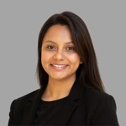 Elvia Jimenez Ciriaco smiling, with long straight dark hair, wearing a black blazer and dark top against a gray background.