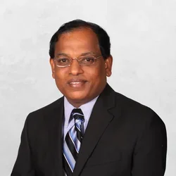 Dr. Pachiyappan Kamarajan is wearing a black suit jacket, a light blue dress shirt, and a striped tie with shades of black, blue, and white.