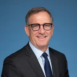 Paul Krebabach smiling and wearing a suit, against a blue background