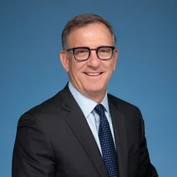 Paul Krebabach smiling and wearing a suit, against a blue background