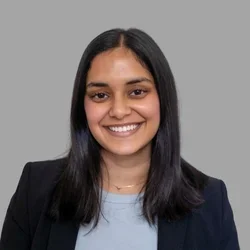 Abha Patkar smiling, with shoulder-length dark hair, wearing a dark blazer over a light top against a gray background.