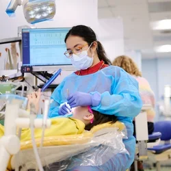 Dentist treating a child patient, who is holding a mirror