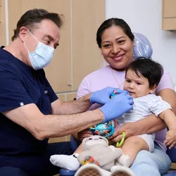 Dr. Francisco Ramos-Gomez administering care to a toddler patient seated on his mother's lap
