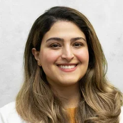 Dr. Pegah Khazaei is wearing a white medical coat layered over a sweater.